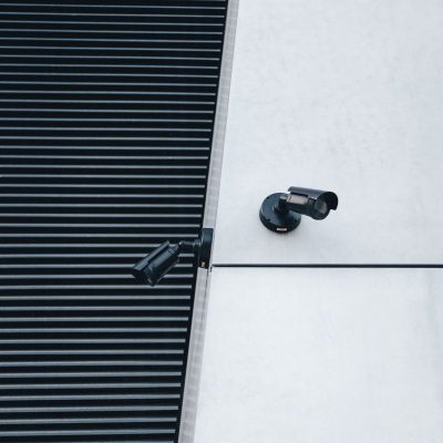 Par de c&acirc;meras de seguran&ccedil;a CFTV modernas instaladas em parede de pr&eacute;dio comercial - Nunes Consultoria Inform&aacute;tica