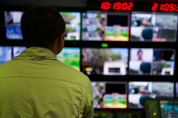 Sala de controle com monitores de CFTV Homem monitorando múltiplas telas de câmeras de segurança em sala de controle - Nunes Consultoria Informática