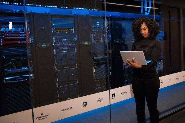 Profissional de TI ao lado de racks de servidor Profissional de TI com notebook ao lado de racks de servidor - Nunes Consultoria Informática